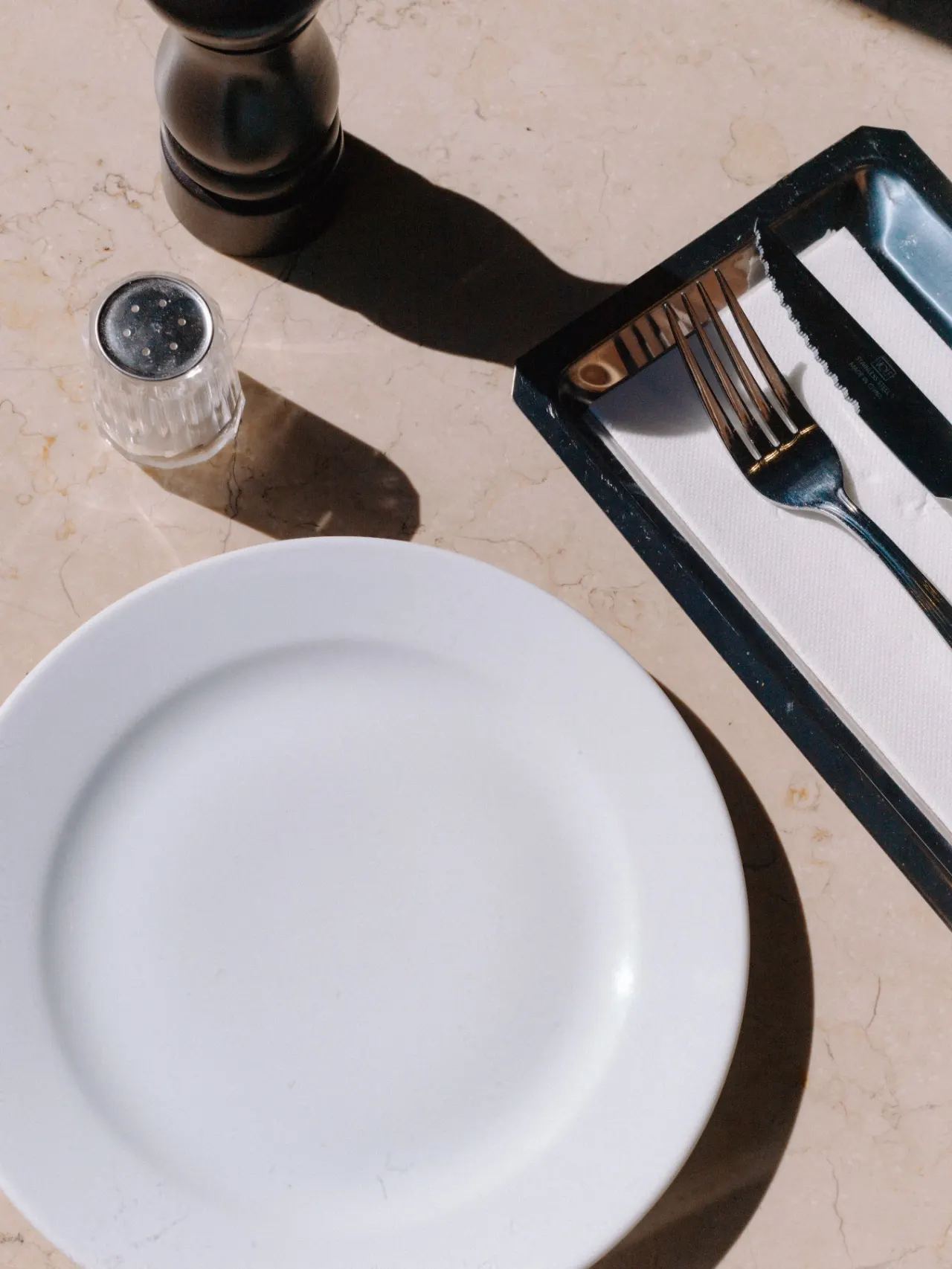 An empty white plate and cutlery on a sunlit table