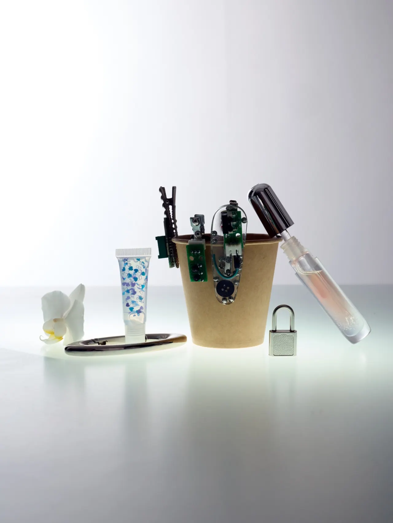 A still life of a paper cup with parts, a padlock and a tube